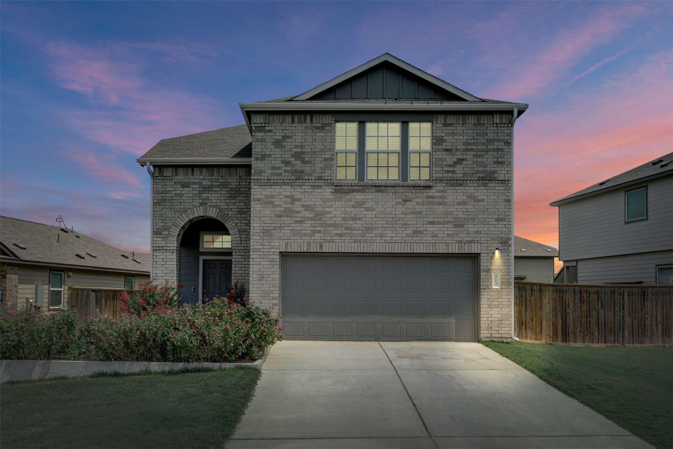 A classic brick exterior with an inviting arched entryway, a large two-car garage, and a lush front garden.