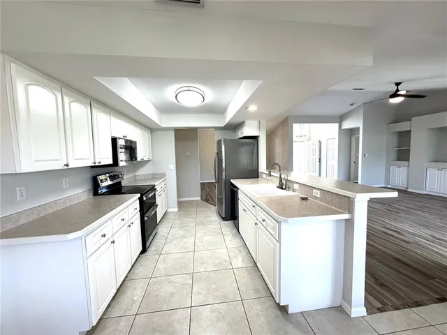 a large white kitchen with a stove top oven a sink dishwasher and white cabinets with wooden floor
