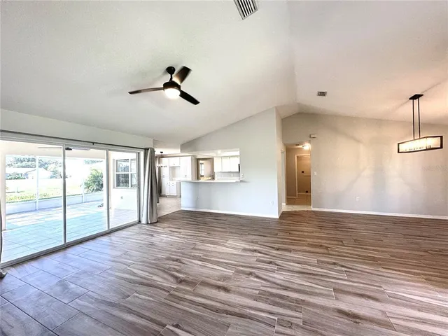 an empty room with wooden floor fan and windows