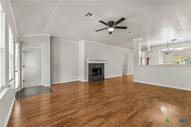 an empty room with wooden floor a ceiling fan and windows