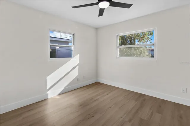 a view of an empty room with wooden floor and a ceiling fan