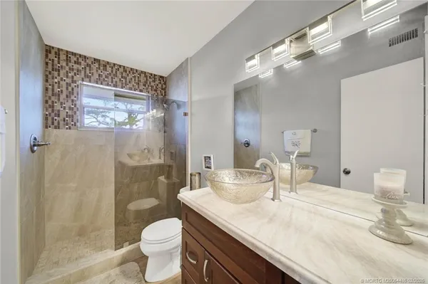 a bathroom with a granite countertop sink a toilet a mirror and shower