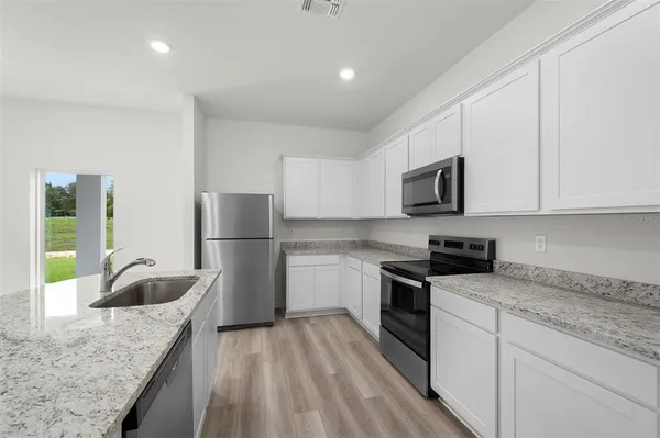 a kitchen with granite countertop a sink a stove top oven a refrigerator and white cabinets