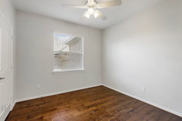 an empty room with wooden floor chandelier fan and windows
