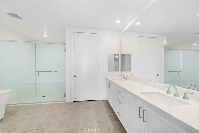 a large white bathroom with a double vanity sink a large mirror and a bathtub