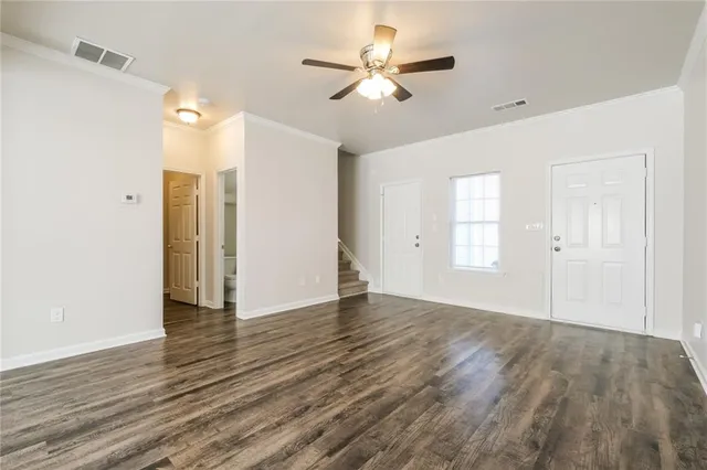 a view of an empty room with wooden floor and a ceiling fan