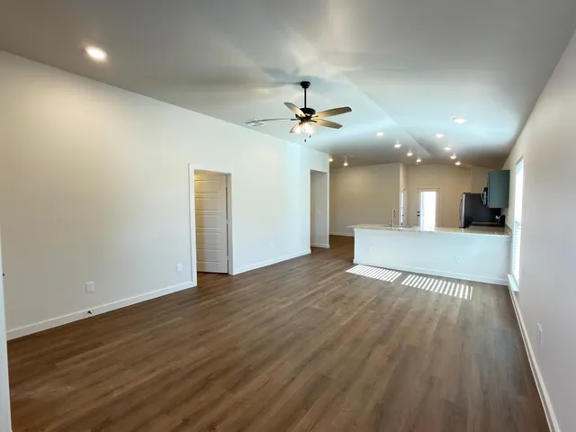 a view of an empty room with wooden floor and a kitchen