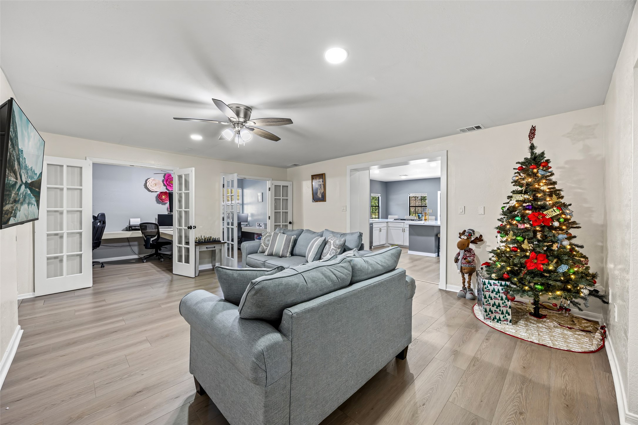 15080 Usher Lane Splendora, TX 77372 - Photo 37 of 44 This inviting living area features modern wood flooring, a cozy seating arrangement, and ample natural light. French doors lead to a separate office space, while an open doorway connects to a bright kitchen. A decorated Christmas tree adds a festive touch.