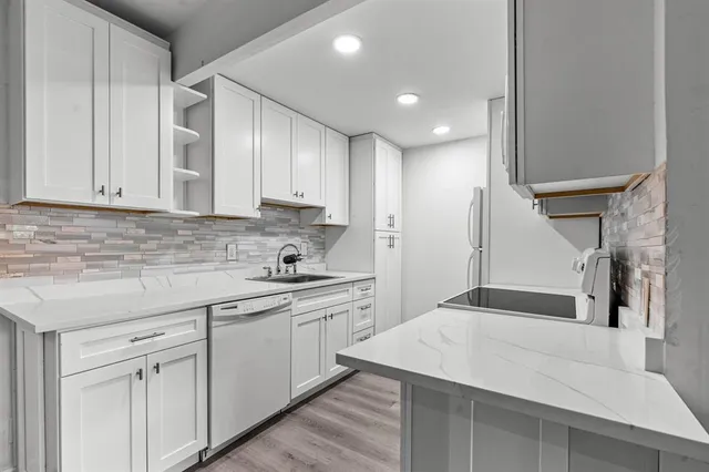 a kitchen with a sink dishwasher and white cabinets with wooden floor