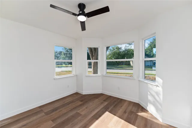 an empty room with wooden floor fan and windows