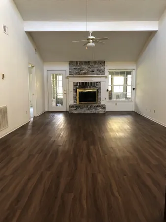 an empty room with wooden floor fireplace and windows