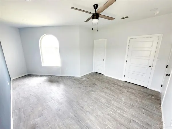 an empty room with wooden floor ceiling fan and windows