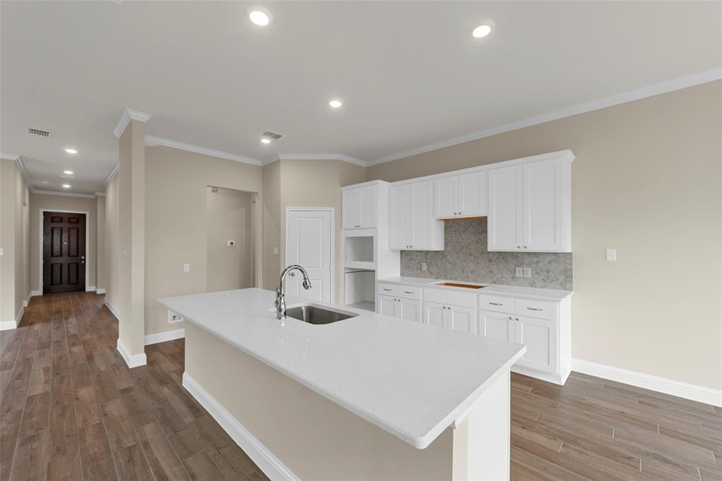 1508 Addison Lane Lancaster, TX 75134 - Photo 2 of 20 Bright kitchen featuring white cabinetry, a large center island with an undermount sink, quartz countertops, a tiled backsplash, and recessed lighting
