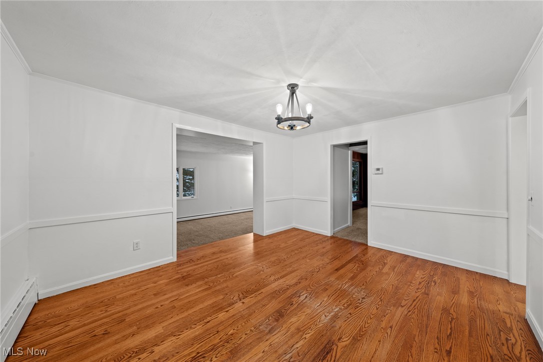 9513 Booth Road Willoughby, OH 44094 - Photo 14 of 45 Spare room featuring a chandelier, hardwood / wood-style floors, baseboard heating, and crown molding