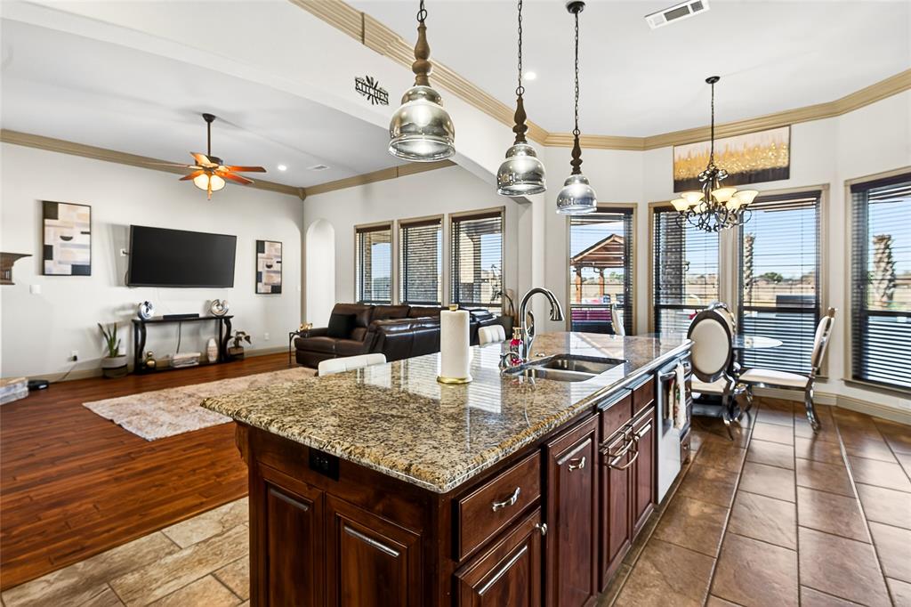 12099 Briargrove Lane Forney, TX 75126 - Photo 38 of 38 Kitchen with dark wood finish cabinetry, crown molding, light stone countertops, open floor plan, and suspended lighting