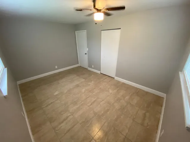 an empty room with a chandelier fan and windows