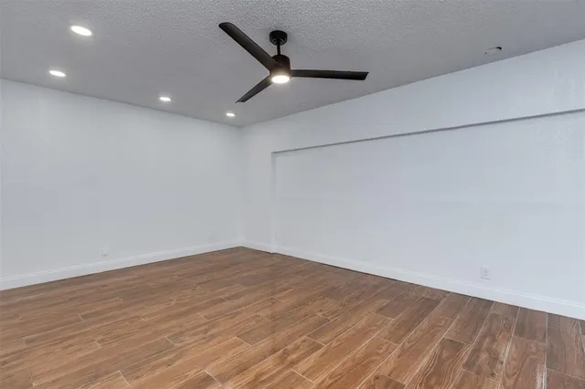 a view of an empty room with wooden floor and a ceiling fan