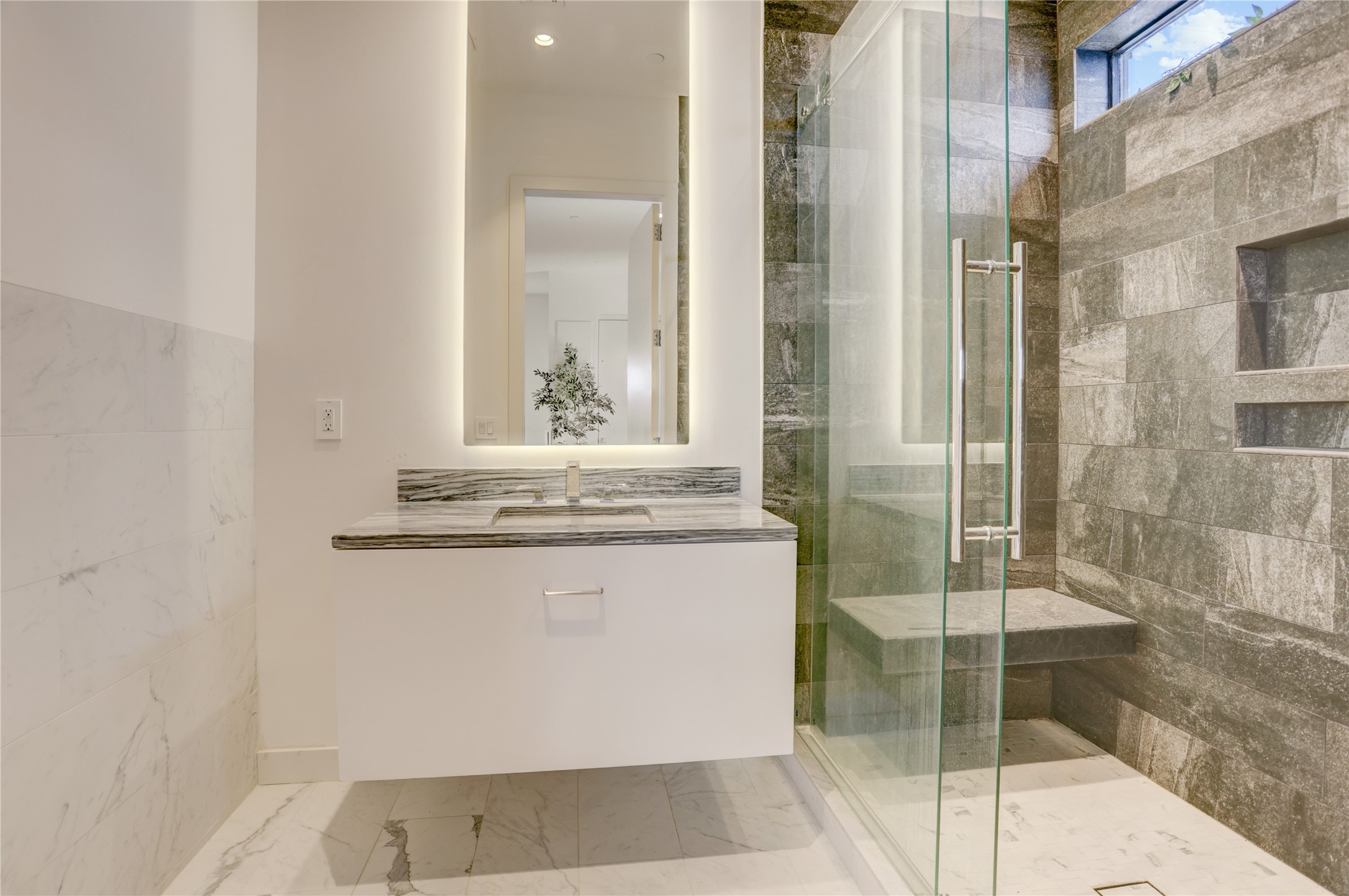 1807 Indiana Street Houston, TX 77006 - Photo 29 of 35 Fourth-Floor Full Bath: Modern top-floor bathroom featuring a white floating vanity with marble countertops, a vertical backlit LED mirror, and a seamless glass walk-in shower finished in striking dark stone tile with an integrated bench.