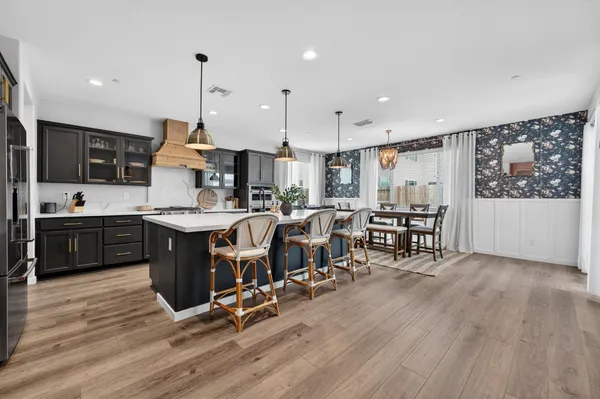 a open kitchen with stainless steel appliances kitchen island granite countertop a dining table chairs and granite counter tops