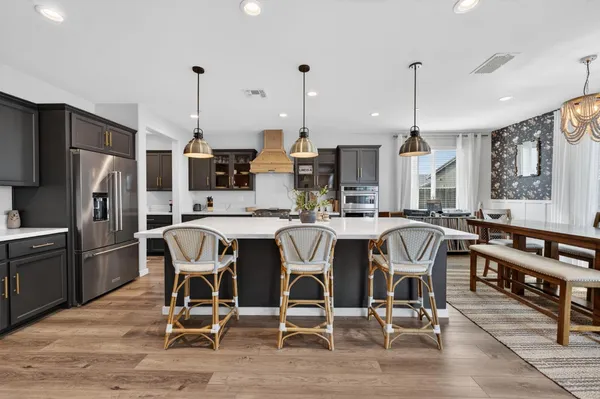 a kitchen with stainless steel appliances kitchen island granite countertop a stove a refrigerator a kitchen island a dining table and chairs with wooden floor