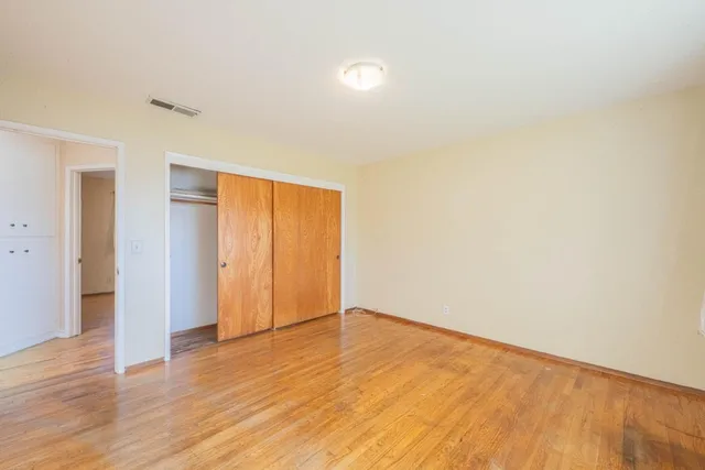 a view of an empty room with wooden floor and closet