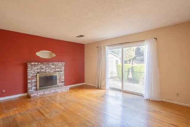 an empty room with wooden floor fireplace and windows