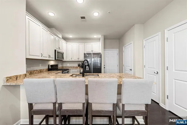 a kitchen with kitchen island granite countertop a dining table chairs refrigerator and cabinets