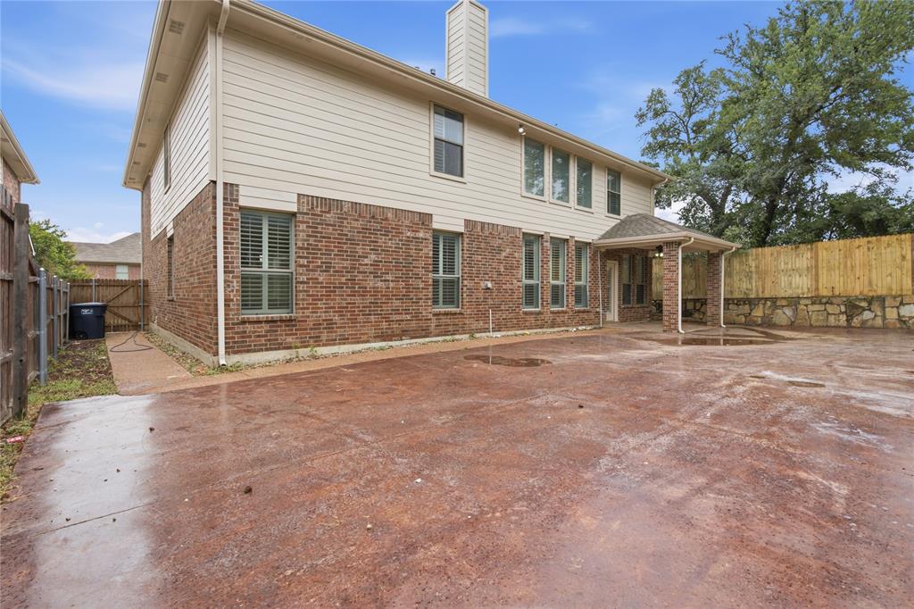 10001 Thurman Road Fort Worth, TX 76244 - Photo 33 of 40 Rear exterior featuring a covered patio, brick and siding facade, multiple windows with louvered blinds, a privacy fence, and a stone retaining wall