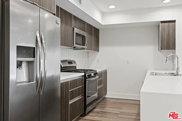 a kitchen with stainless steel appliances granite countertop a refrigerator a stove and a sink with wooden floor