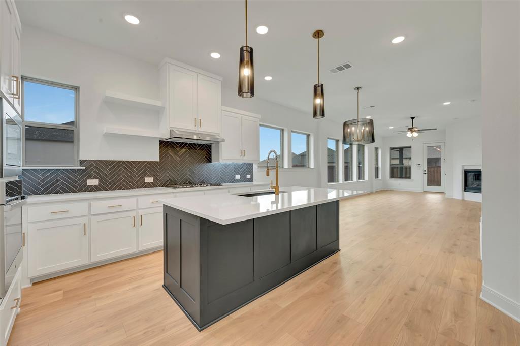 1856 Lightner Road Van Alstyne, TX 75495 - Photo 11 of 33 Modern kitchen featuring white cabinetry, a dark herringbone tile backsplash, and a large central island with a light-colored countertop