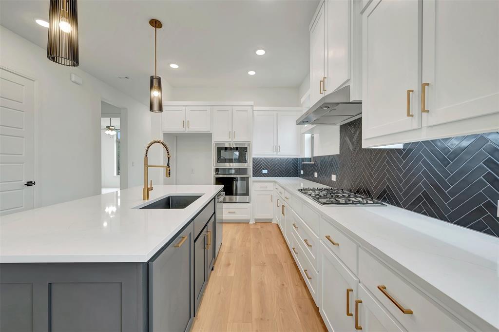 1856 Lightner Road Van Alstyne, TX 75495 - Photo 14 of 33 Kitchen featuring a large island with an undermount sink and a brass-finish faucet, white cabinetry, integrated stainless steel appliances, a five-burner gas cooktop, and a dark herringbone tile backsplash
