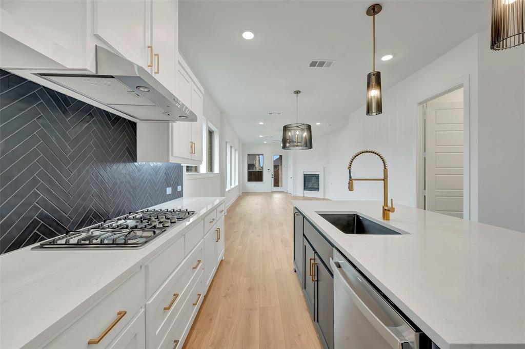 1856 Lightner Road Van Alstyne, TX 75495 - Photo 15 of 33 Modern kitchen featuring a gas range, herringbone tile backsplash, white cabinetry with brass hardware, and an island with a built-in sink and gold-tone faucet