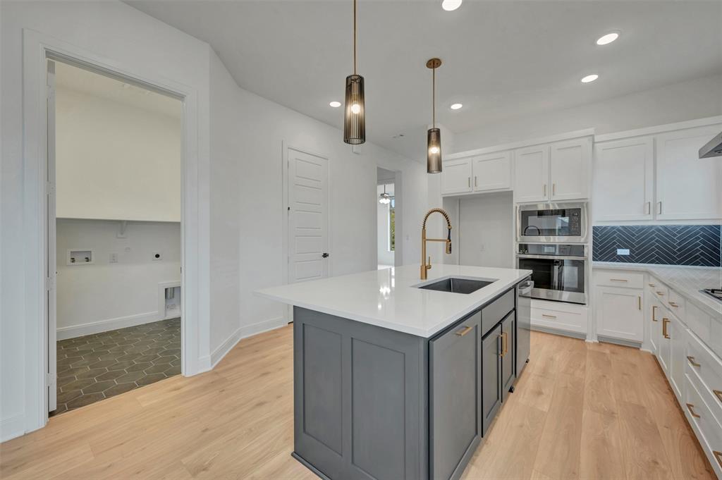 1856 Lightner Road Van Alstyne, TX 75495 - Photo 17 of 33 Modern kitchen featuring a central island with a dark gray base and white countertop, equipped with an undermount sink and a brass-finish faucet
