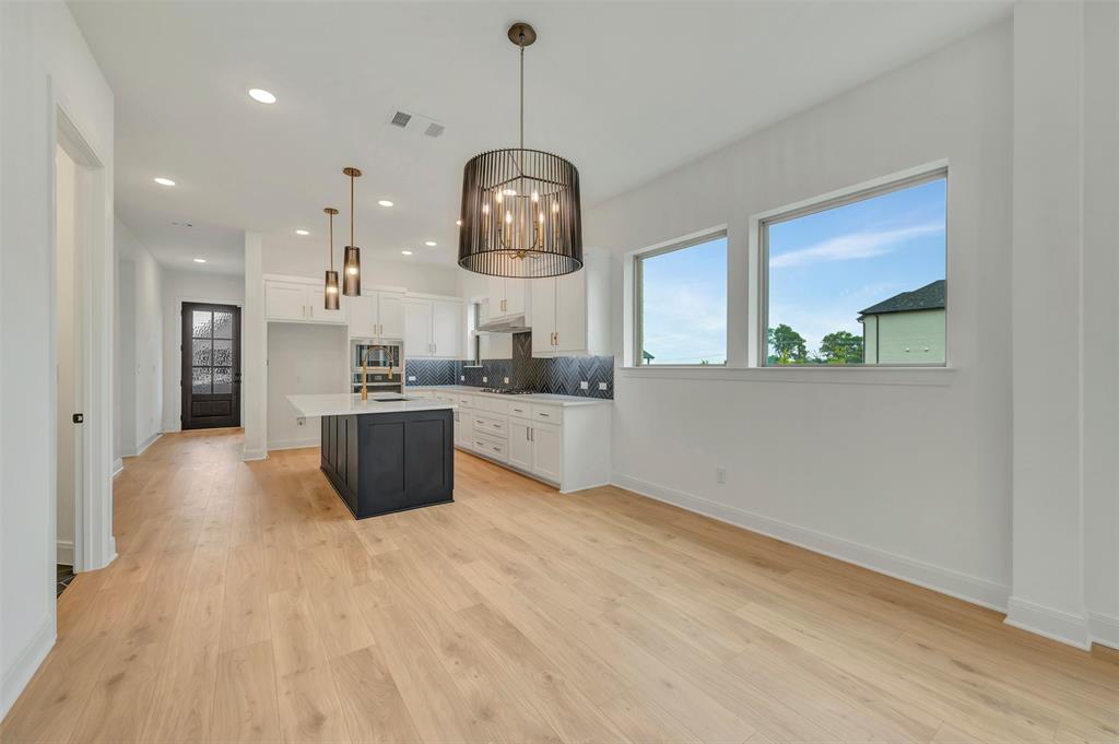 1856 Lightner Road Van Alstyne, TX 75495 - Photo 21 of 33 Open-concept living space featuring wood-finish flooring, a modern kitchen with a dark-toned island, pendant lighting, built-in appliances, and multiple windows