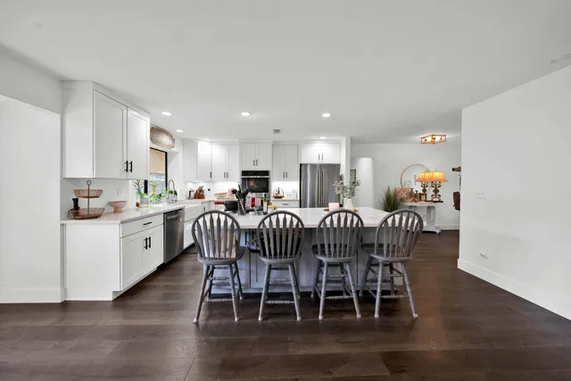 a living room with stainless steel appliances furniture wooden floor and a kitchen view