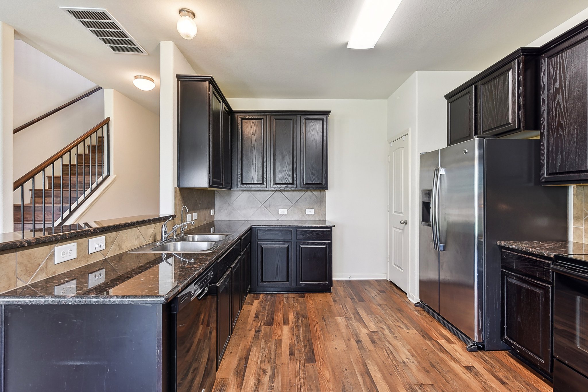 310 Potters Peak Way Georgetown, TX 78626 - Photo 3 of 21 Kitchen featuring wood-finish flooring, dark cabinetry, stainless steel appliances, and stone countertops