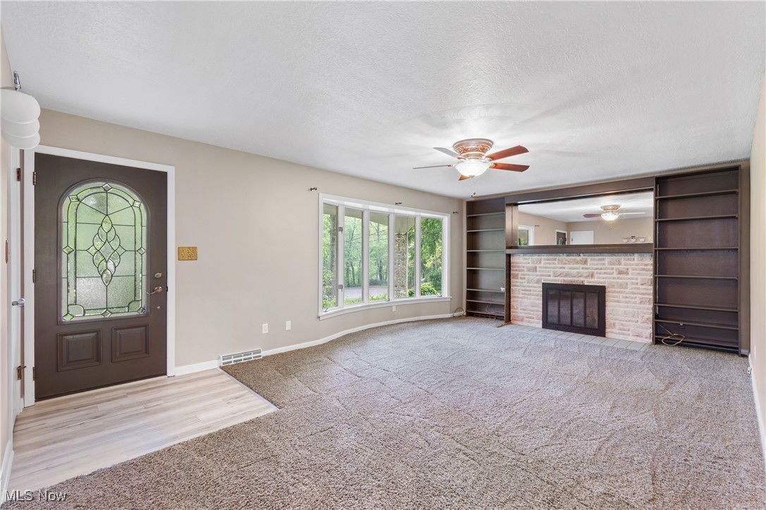 3143 Ethan Allen Road Barberton, OH 44203 - Photo 6 of 37 Unfurnished living room with healthy amount of natural light, ceiling fan, carpet, a textured ceiling, and a stone fireplace