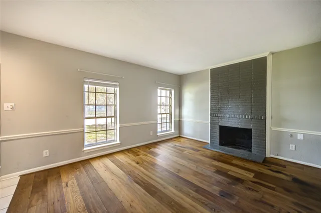 an empty room with wooden floor fireplace and windows