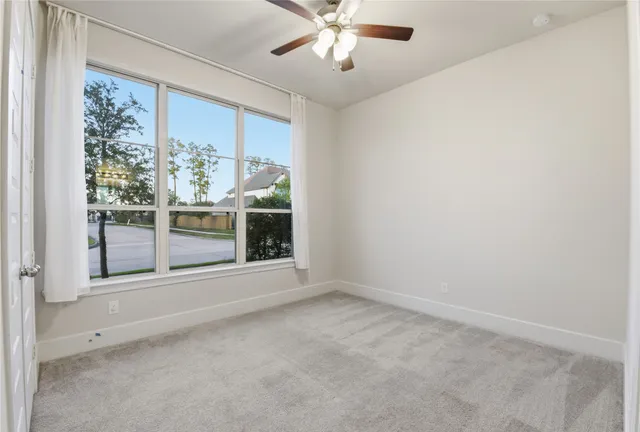 an empty room with chandelier fan and kitchen view