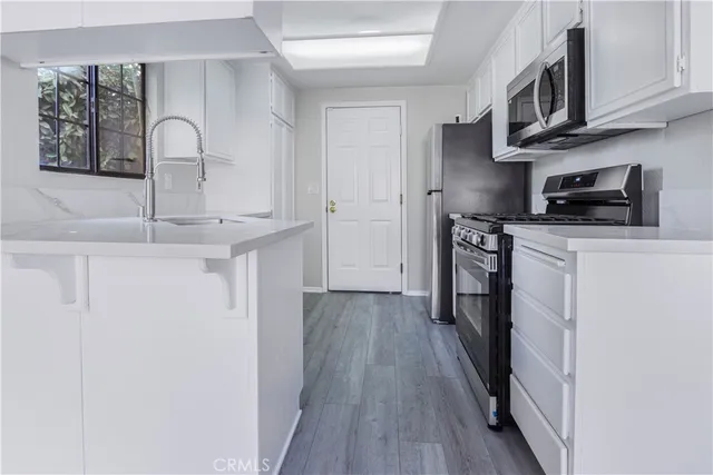 a kitchen with stainless steel appliances granite countertop a stove top oven a sink dishwasher and white cabinets with wooden floor