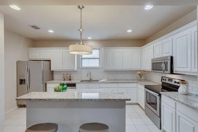 a kitchen with granite countertop stainless steel appliances a sink a stove a refrigerator cabinets and chairs