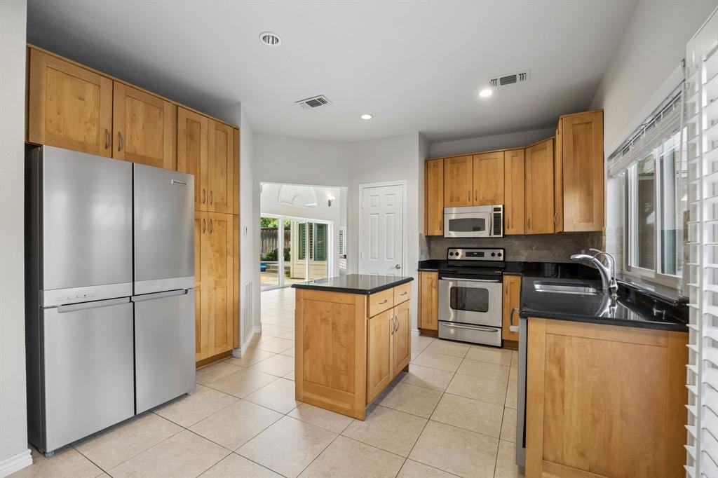 4115 Rive Lane Addison, TX 75001 - Photo 7 of 25 Kitchen featuring ample wood cabinetry, dark countertops, stainless steel appliances, a central island, and tiled flooring