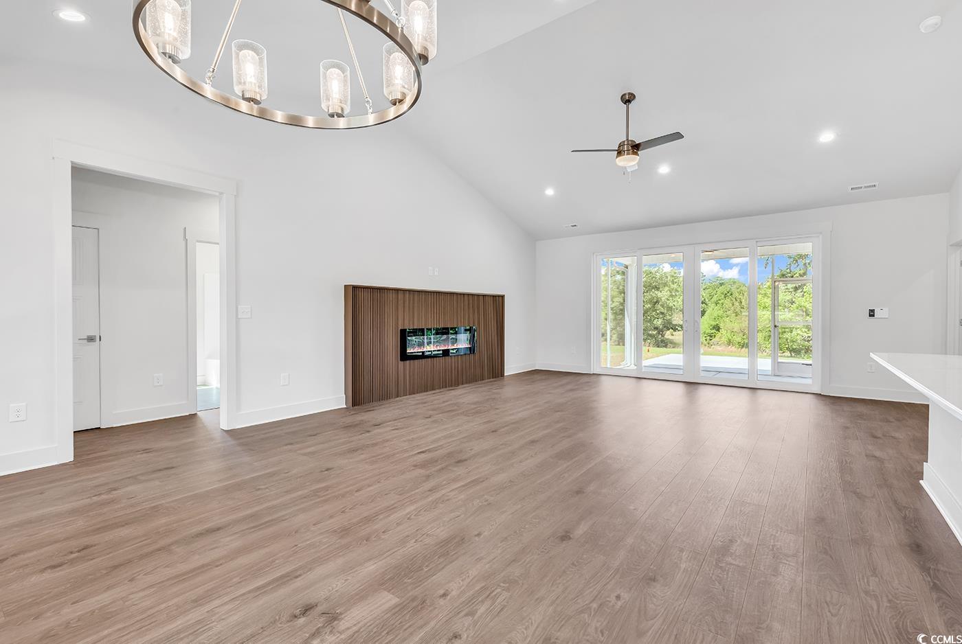718 Highway 348 Loris, SC 29569 - Photo 10 of 28 Unfurnished living room featuring high vaulted ceiling, a glass covered fireplace, ceiling fan, with notable Dining area chandelier, wide baseboards and door trim, and wood laminate flooring