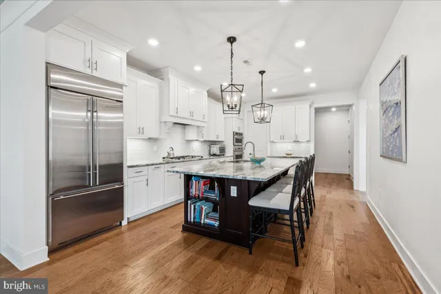 a kitchen with stainless steel appliances granite countertop a refrigerator a sink dishwasher a stove and white cabinets with wooden floor