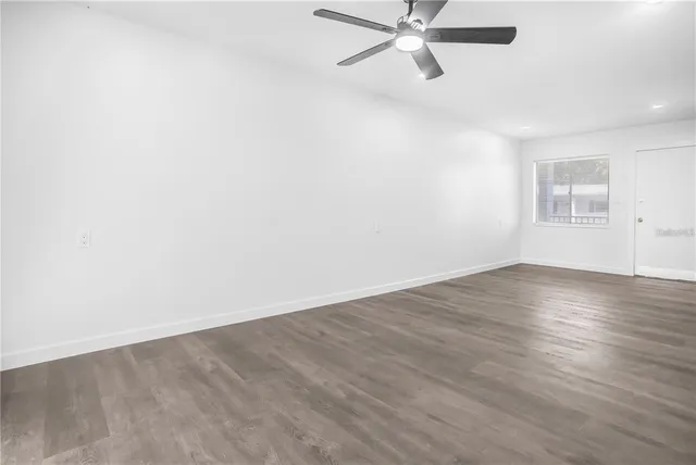 an empty room with wooden floor fan and windows