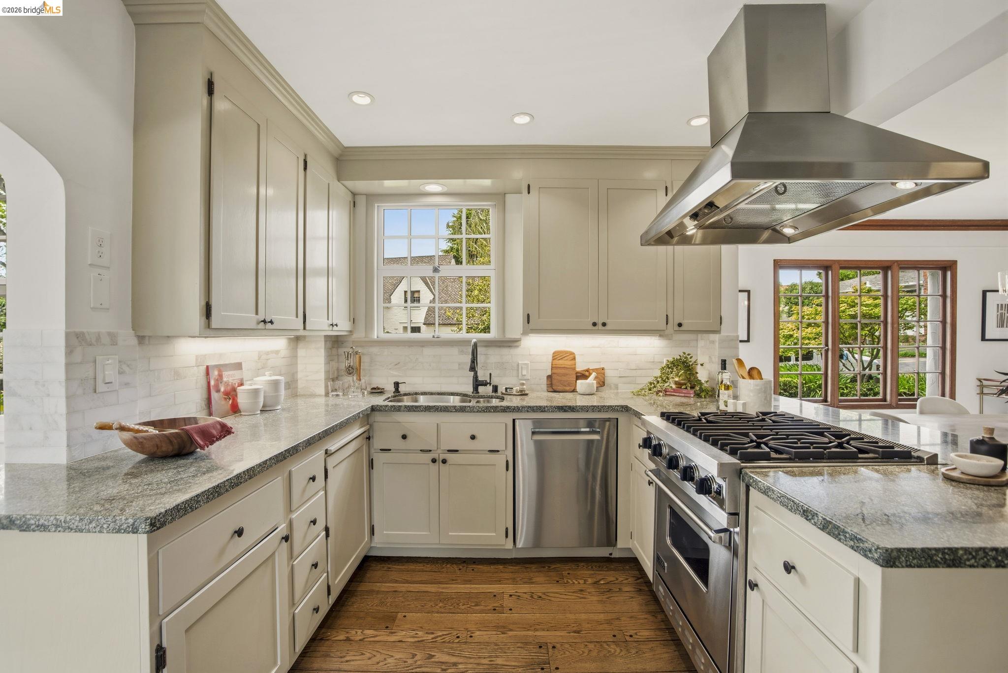 1087 Hubert Road Oakland, CA 94610 - Photo 16 of 67 Gourmet kitchen featuring a professional-grade range, stainless steel appliances, granite countertops, white shaker cabinetry, and wood-finish flooring