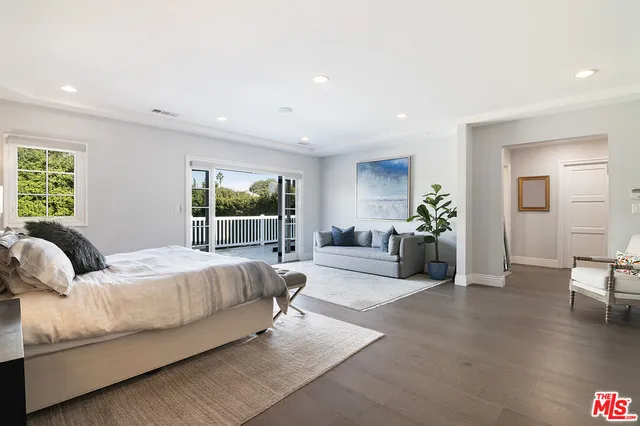 a bedroom with a large bed and potted plant with wooden floor