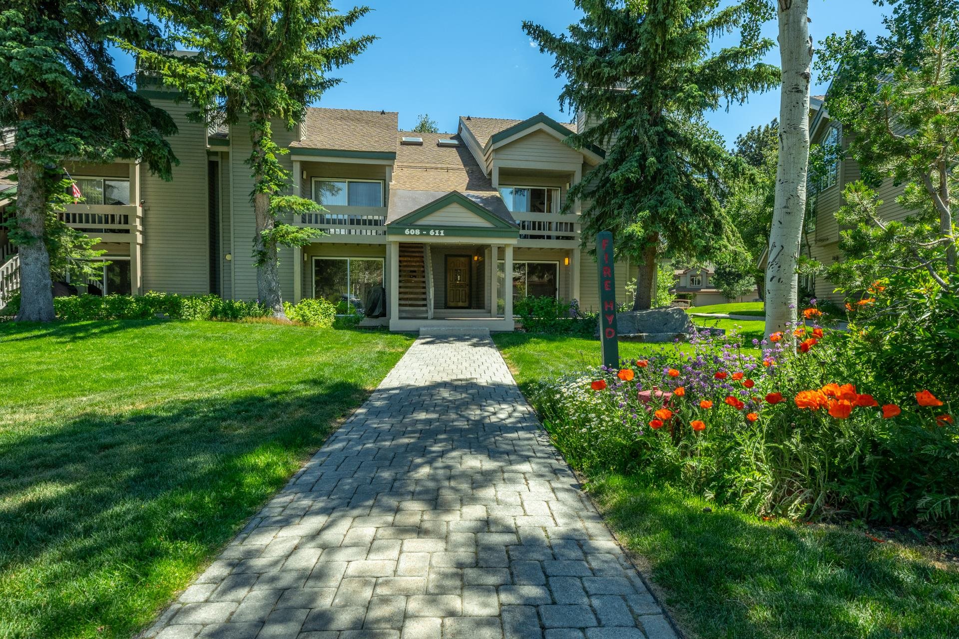609 Golden Creek Road, Unit 609 Mammoth Lakes, CA 93546 - Photo 1 of 42 Multi-story residence featuring a brick paver walkway, manicured lawn, established trees, vibrant floral landscaping, and covered entryways