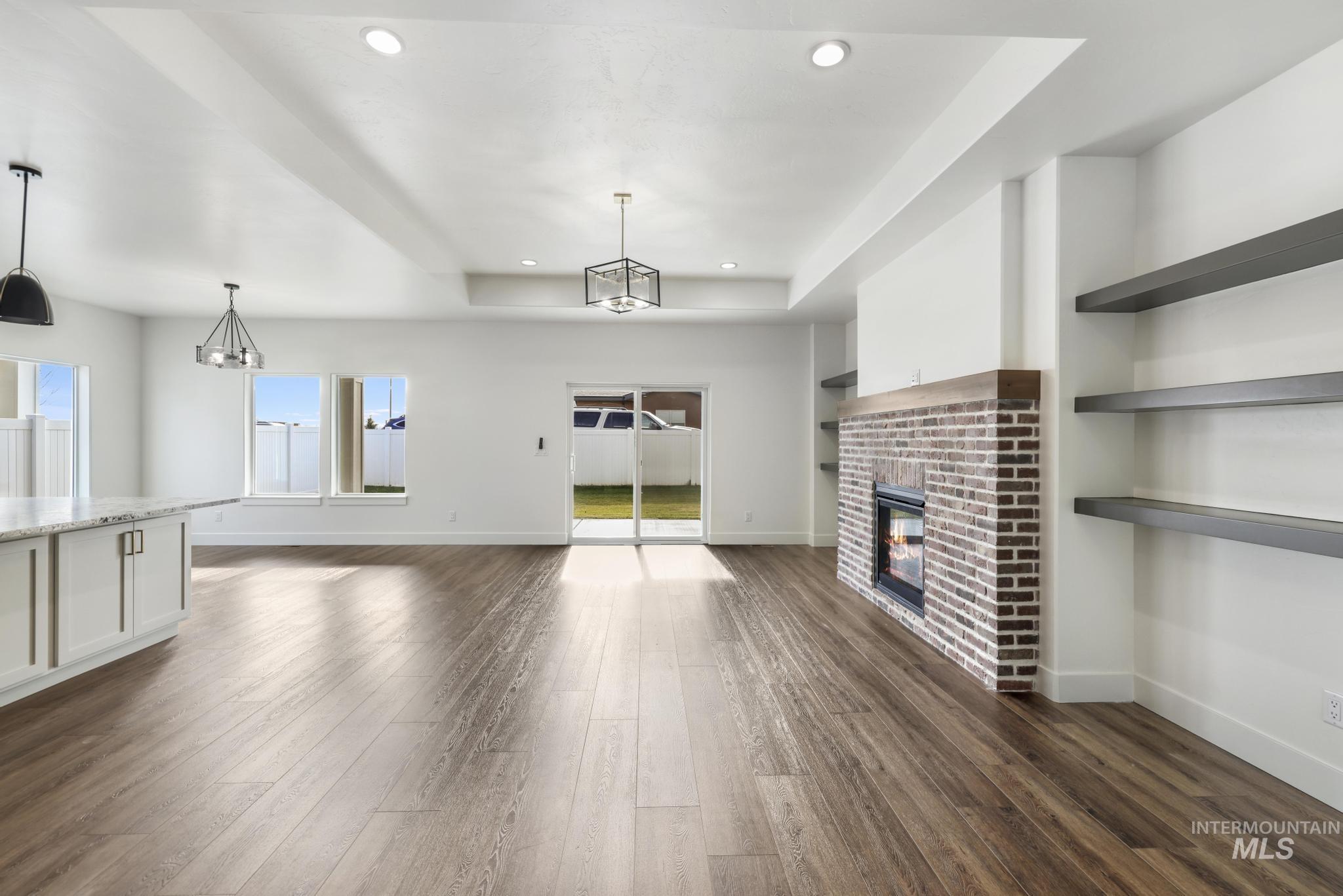 527 Falling Leaf Lane Twin Falls, ID 83301 - Photo 11 of 42 Unfurnished living room with a brick fireplace, dark wood-style flooring, recessed lighting, and a tray ceiling