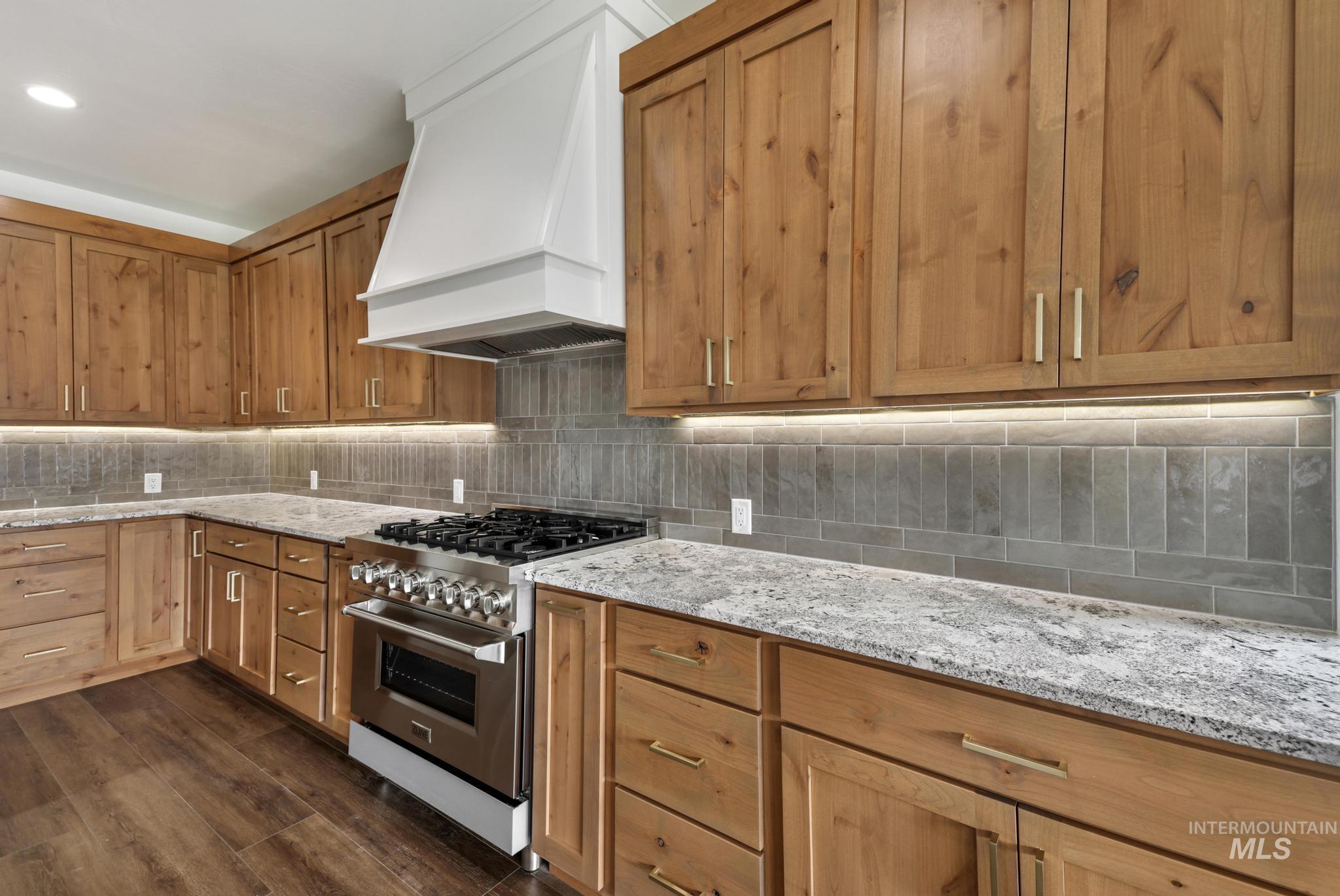 527 Falling Leaf Lane Twin Falls, ID 83301 - Photo 12 of 42 Kitchen with stainless steel range, premium range hood, light stone counters, tasteful backsplash, and brown cabinetry
